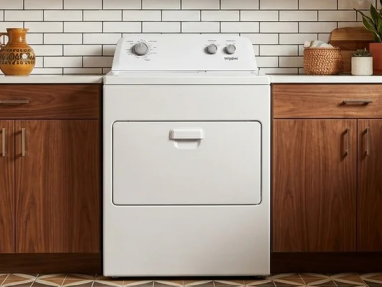 A white electric dryer between wooden cabinets in front of a subway-tile wall