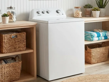 A white top-load washer between wooden shelves holding woven baskets and folded towels